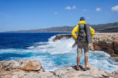 Sırt çantalı bir adam kayalık bir uçurumda duruyor ve Akdeniz 'deki fırtınaya bakıyor.