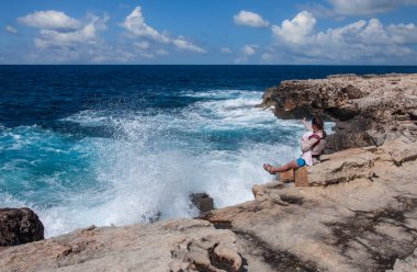 Taştan bir uçurumun kenarında oturan çocuklu genç bir kadın Akdeniz 'deki fırtınaya bakıyor.