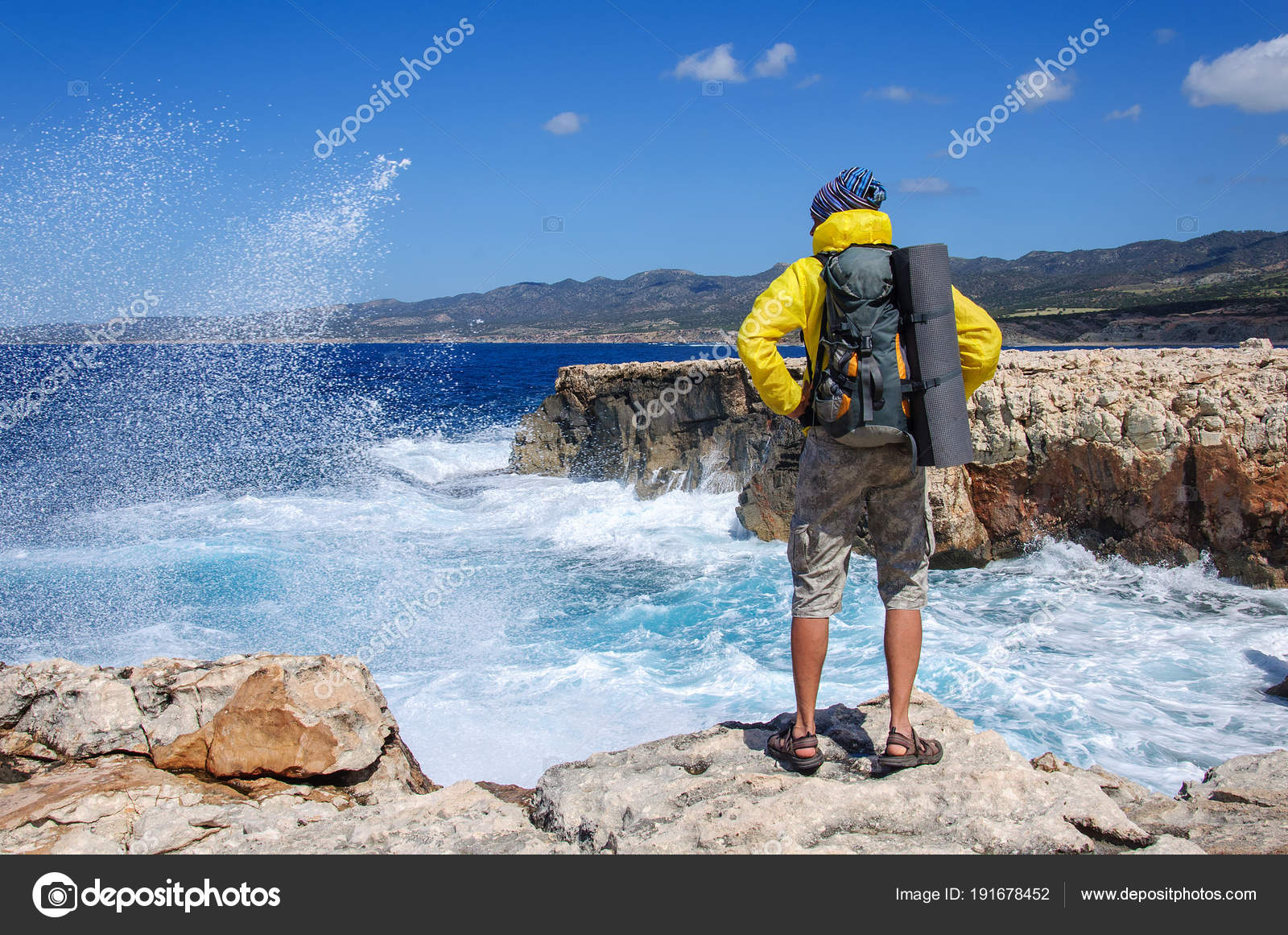 Hombre con una mochila de pie en un precipicio de piedra y mira a