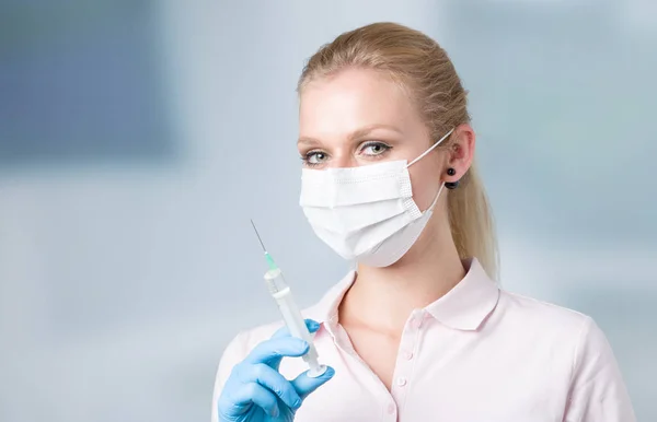 Young female doctor with injection needle and medica face mask — Stock Photo, Image