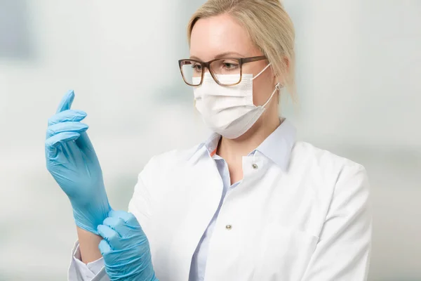 female doctor with medical face mask puts on medical gloves