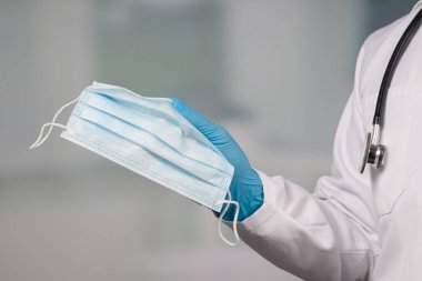 Doktorun elinin tıbbi eldivenlerle kapatılması enfeksiyondan korunmak için tıbbi yüz maskesi gösteriyor. 