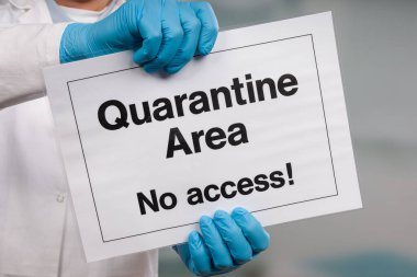 Doktorun elinde tıbbi eldiven var. Yasak bölgenin önünde karantina işareti var.