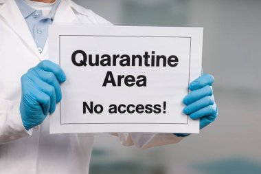 Doktorun elinde tıbbi eldiven var. Yasak bölgenin önünde karantina işareti var.