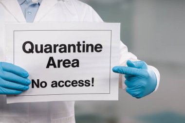 Doktorun elinde tıbbi eldiven var. Yasak bölgenin önünde karantina işareti var.