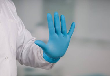 Klinik odasının önünde tıbbi eldiven giyip el hareketlerini durdurarak.