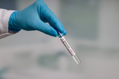 Virüs analizinden sonra laboratuvar odasının önünde test tüpü tutan mavi eldivenleri teslim et.
