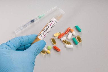 Tıbbi eldivenlerin içinde bir Coronavirus test tüpü var. Sonuç işaretleyicisi, ilaç hapları ve arka planda bir şırınga var.