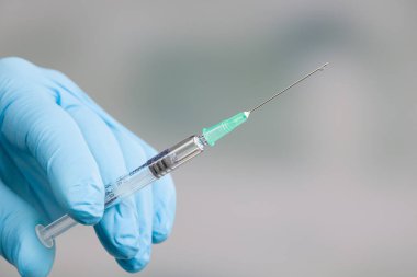Doktorun elini tıbbî eldivenlerle kapat. Elinde bir damla serum olan bir şırınga var.