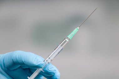 Ellerinde aşı olan bir şırınga tutan tıbbi eldivenlerle doktorun elini kapat.