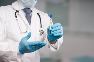 Doktorun elinde virüs analizinden sonra laboratuvar odasının önünde test tüpü var.  