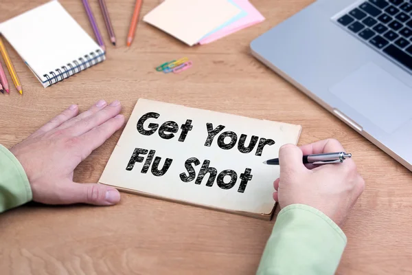 Hand writing Get Your Flu Shot. Office desk with a laptop and st