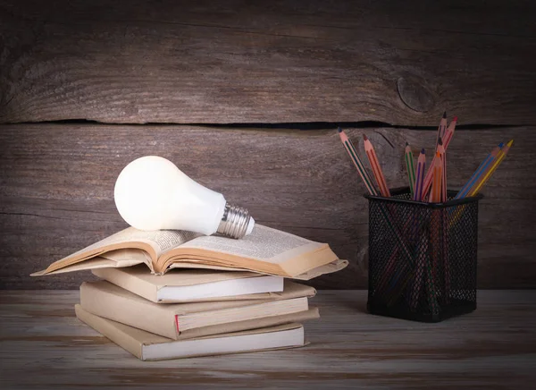 Stapel boeken, gloeilamp en potloden op de houten tafel — Stockfoto