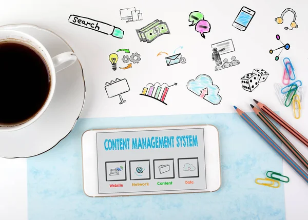 Content Management System concept. Mobile phone and coffee cup on a white office desk