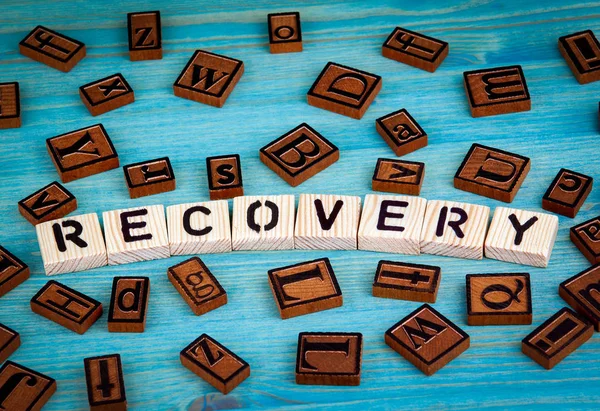 recovery word written on wood block. Wooden alphabet on a blue background