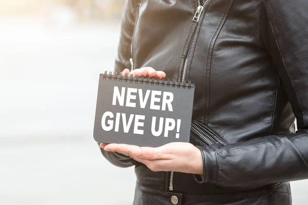 NEVER GIVE UP. Woman holding black notebook with text