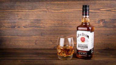 Bir şişe Jim Beam Bourbon ve ahşap arka planda buzlu bir bardak.
