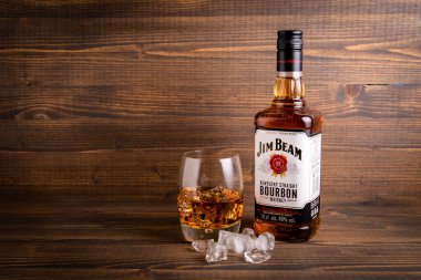 Bir şişe Jim Beam Bourbon ve ahşap arka planda buzlu bir bardak.