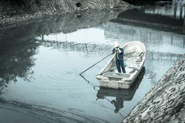 Filtrelenmiş görüntü kadın işçisi teknede kirli bir nehri temizliyor.