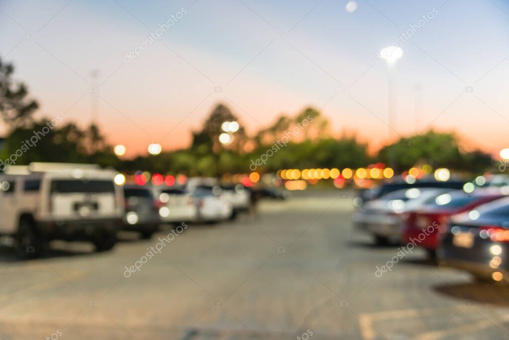 Abstract blurred parking lot of modern shopping center in Houston, Texas, USA. Exterior view mall complex with row of cars in outdoor uncovered parking, bokeh light poles in background