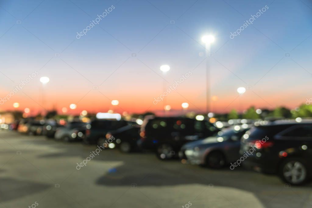 Abstract blurred parking lot of modern shopping center in Houston, Texas, USA. Exterior view mall complex with row of cars in outdoor uncovered parking, bokeh light poles in background