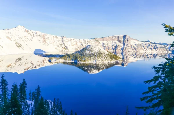 Large snow cliff and pine trees lush in Crater Lake with snowcap mountain and Wizard island reflection — Stock Photo, Image