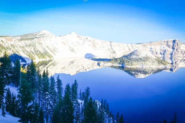 Large snow cliff and pine trees lush in Crater Lake with snowcap mountain and Wizard island reflection — Stock Photo, Image