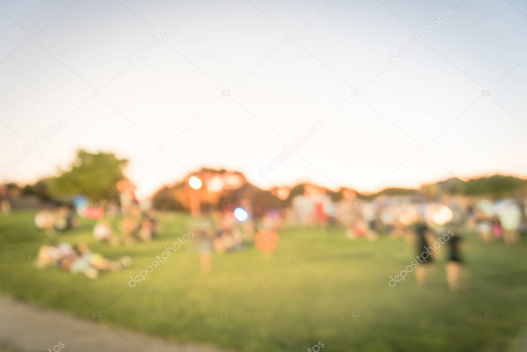 Blurred motion crowed people attending public festival at on green grass lawn of city park near Dallas, Texas, America. Diverse group of family members enjoy summer event at sunset bokeh lighting