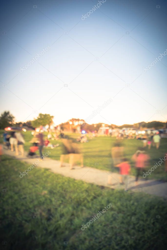 Blurred motion crowed people attending public festival at on green grass lawn of city park near Dallas, Texas, America. Diverse group of family members enjoy summer event at sunset bokeh lighting