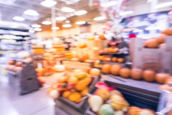 Blurred image Halloween decoration inside grocery store in Houston, Texas, USA. Pile of pumpkins on hay, corns, garden cart wagon and scarecrow on display. Holiday festive background.