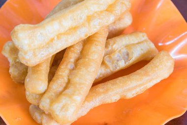 Lezzetli portakal tabağı Youtiao veya kek veya Çin hamur tatlısı, kızarmış ekmek, börek, yağ çubuğu, donut, ahşap masa. Vietnam mutfağında erişte ve çorbayla servis edilir..
