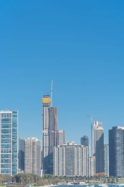 View to Chicago downtown from Lake Michigan with building density. Row of new and under construction skyline with working crane, yacht boats on foreground water