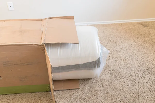 在美国得克萨斯州公寓卧室的地毯地板上 可欣赏到全新的卷包装弹簧床垫 泡沫和乳胶混合材料床垫从纸板箱中脱箱 — 图库照片