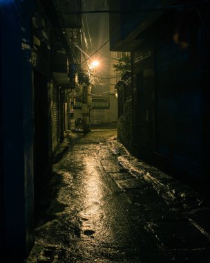 Klasik ton, karanlık, gölgeli ve tehlikeli görünen şehir arka sokağı gece vakti Hanoi, Vietnam 'da. Uzun yolun sonundaki lambanın ıslak kaldırımına alçak ışık yansıyor.