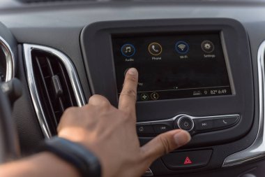 Close-up view of Asian male hand touching screen in modern car. Left hand wears a black smart watch adjust LCD dashboard system control interface on black car interior clipart