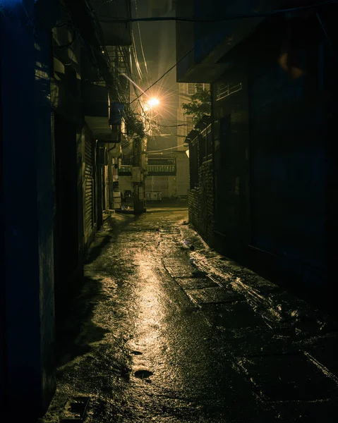 Klasik ton, karanlık, gölgeli ve tehlikeli görünen şehir arka sokağı gece vakti Hanoi, Vietnam 'da. Uzun yolun sonundaki lambanın ıslak kaldırımına alçak ışık yansıyor.