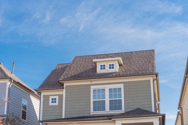 Dormer roof windows on second story of typical home in suburbs Dallas, Texas, USA. Close-up outside loft attic space with weathered shingle siding of residential house under cloud blue sky