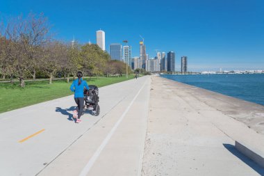 Arka planda şehir Chicago siluetleri ile Michigan Gölü kıyı şeridi boyunca çalışan ve bebek arabası iterek uygun Asya bayan Arka görünüm. Fit spor giyim kadın egzersiz açık sonbaharda gündüz