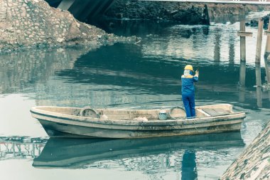 Arkadan bakan kadın işçiler Hanoi 'de kirli su ve çeşitli atıklarla dolu bir kanalı temizliyor. Kirlilik Vietnam 'ın en ciddi sorunlarından biridir. Yüz maskesi ve miğfer takan ekip.
