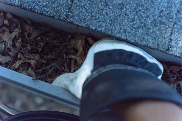 Top view man hand in gloves cleaning house gutter from leaves and dirt. Roof gutter cleaning near shingles roof in summer time