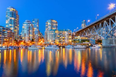 Vancouver Bc gökdelenleri ve Granville Köprüsü mavi saatte False Creek boyunca yansıyor.