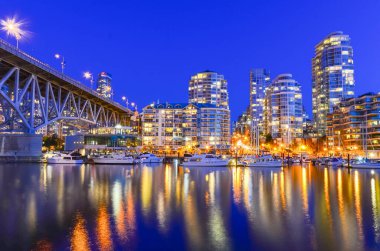 Vancouver Bc gökdelenleri ve Granville Köprüsü mavi saatte False Creek boyunca yansıyor.