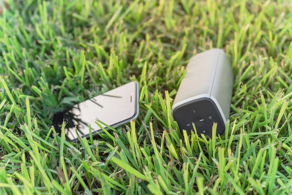 Typical smart phone and Bluetooth speaker on grass lawn nature environment — Stock fotografie