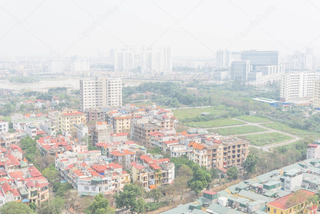 Dense of residential houses and high-rise condominium building in background. Foggy or polluted air is common in Hanoi, Vietnam. Aerial view urban sprawling with red metal roof multistory homes.