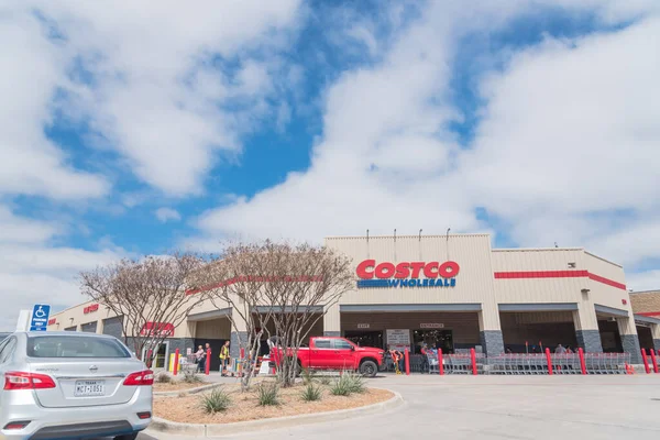 Занятые клиенты, входящие и выходящие из оптового магазина Costco в Льюисвилле, штат Техас, в облачно-голубом небе — стоковое фото