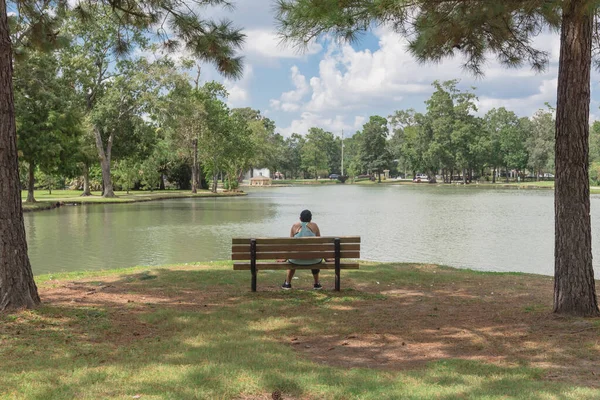 米国テキサス州ヒューストンの湖畔の都市公園のベンチに黒いキャップを持つスポーティな女性をバックビュー — ストック写真