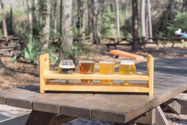 Beer flight sampler tray on wooden picnic table with blurry forest background of brewery in Texas, USA