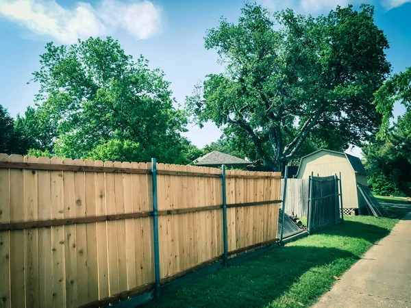 New wooden fence near collapsed slats in backyard of residential house with shed in suburban Dallas
