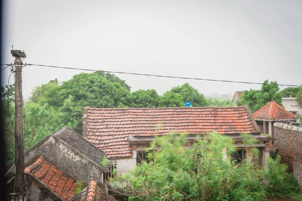 Ancienne maison de toit en tuiles et pylônes en béton sous de fortes pluies et du vent dans un village reculé du nord du Vietnam — Photo