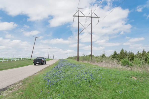 Carro da vista traseira que conduz na estrada do país com flor do bluebonnet e cerca branca do piquete sob a fileira dos pilões do poder em Ennis, Texas, EUA — Fotografia de Stock